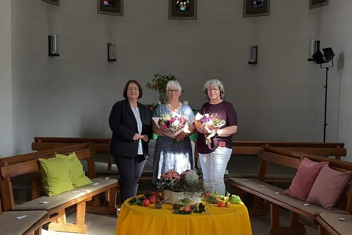 Bettina Lugk (links) steht mit zwei Frauen in einem Raum, die jeweils einen Blumenstrauß halten.