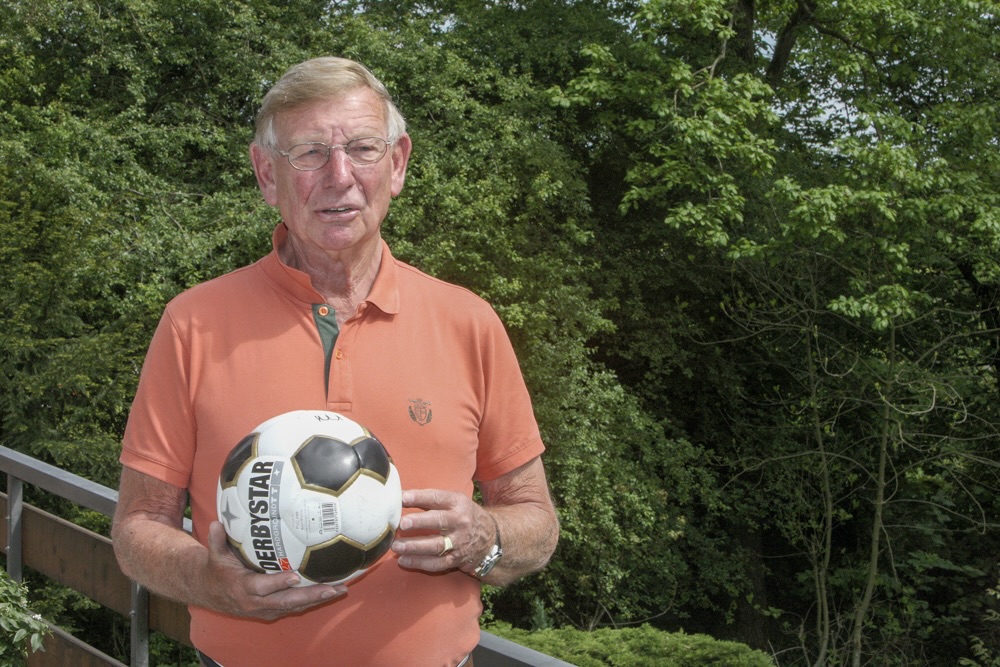 Porträt von Franz-Josef Bomnüter, der einen Fußball hält und lächelt. Im Hintergrund sind Bäume zu sehen.