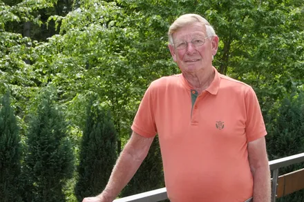 Porträt von Franz-Josef Bomnüter, einem älteren Mann mit Brille und orangefarbenem Poloshirt, vor grünem Hintergrund.