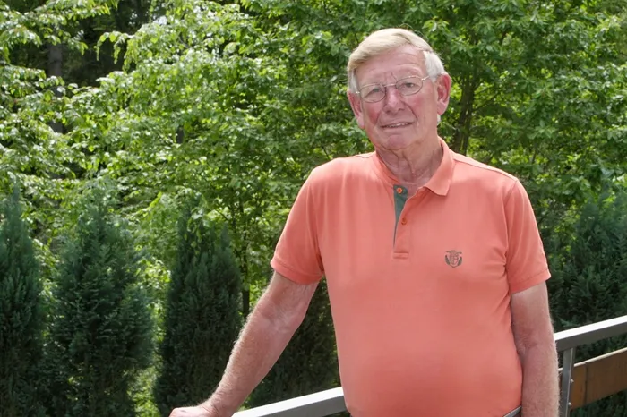 Porträt von Franz-Josef Bomnüter, einem älteren Mann mit Brille und orangefarbenem Poloshirt, vor grünem Hintergrund.