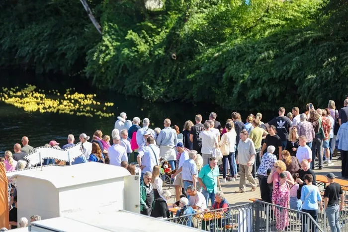 Viele Menschen versammeln sich beim Brückenfest 2026 an einem Gewässer vor einer grünen Waldkulisse.