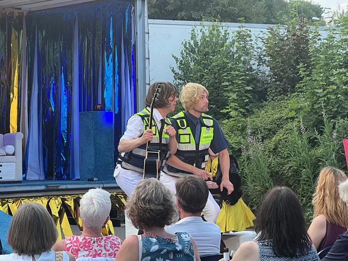 Zwei Männer mit gelben Schwimmwesten und weißen Hosen stehen auf einer Bühne vor einem Publikum. Einer spielt Gitarre, der andere gestikuliert.