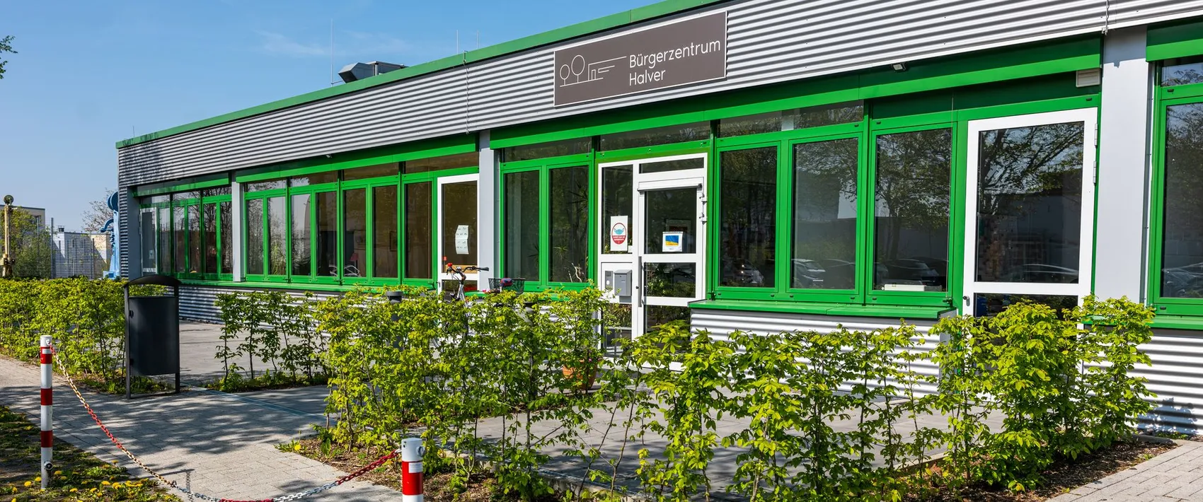Das Bürgerzentrum Halver mit seiner Fassade aus grauem Wellblech und grünen Fensterrahmen. Ein rotes und weißes Absperrband schützt den Eingangsbereich.