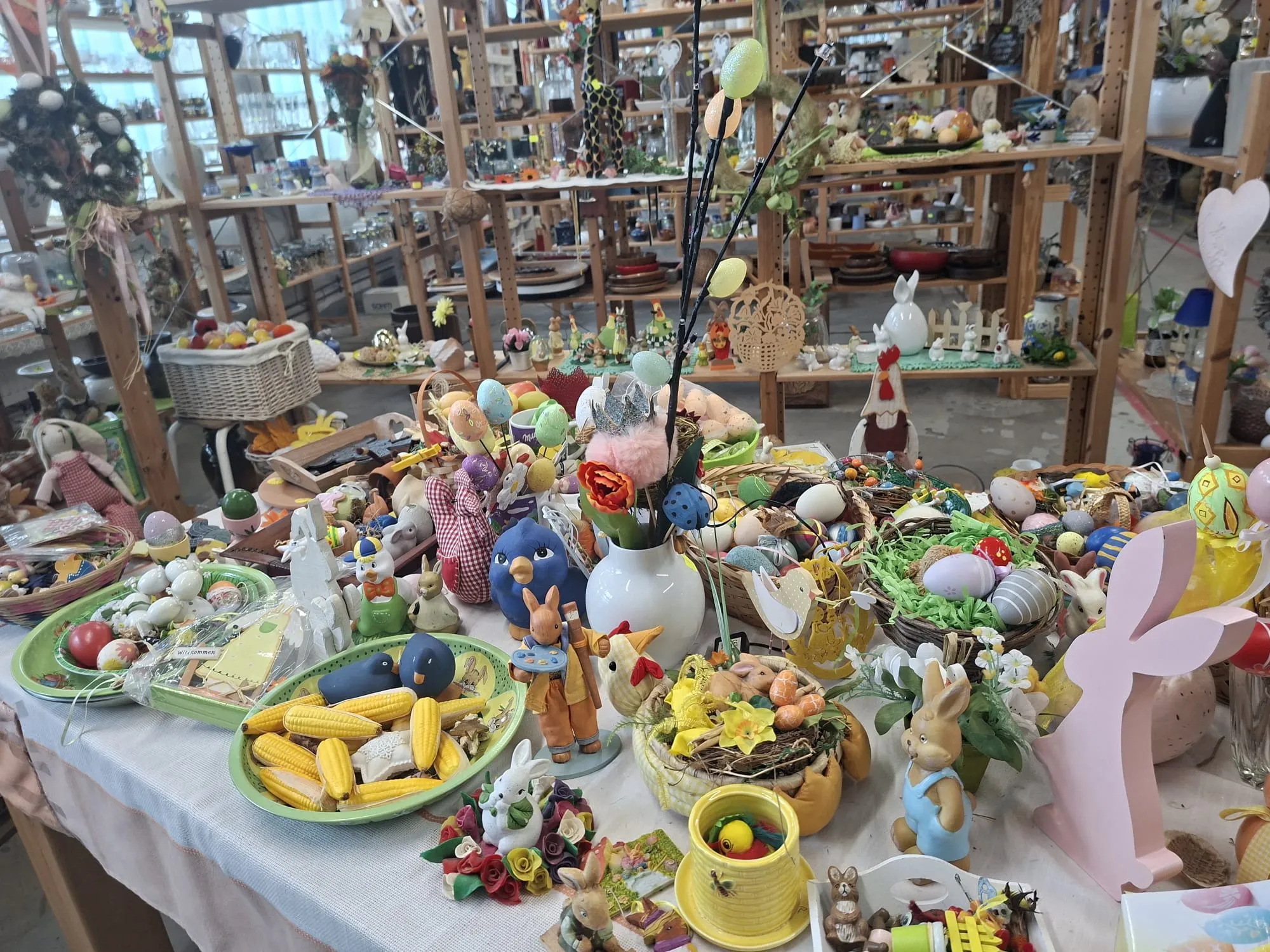 Ein reichhaltig bestückter Stand auf einem Ostereiermarkt mit zahlreichen bunten Ostereiern, Hasenfiguren, Vögeln und Frühlingsdekorationen.