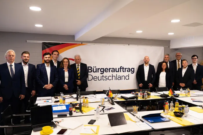 Der Vorstand der Partei Bürgerauftrag Deutschland posiert für ein Gruppenfoto vor einem Banner in einem Konferenzraum.