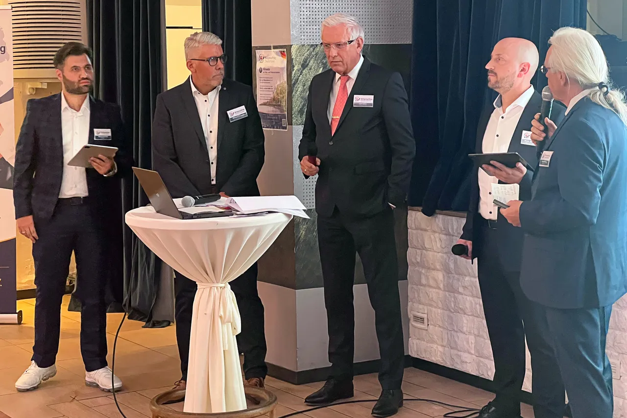 Fünf Männer in Anzügen stehen bei einer Informationsveranstaltung der Partei Bürgerauftrag Deutschland an einem Stehtisch mit Laptop und Unterlagen.