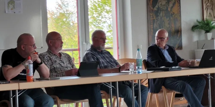 Vier Männer sitzen an einem Tisch während einer Diskussion über Windkraft im Ausschuss für Stadtentwicklung.