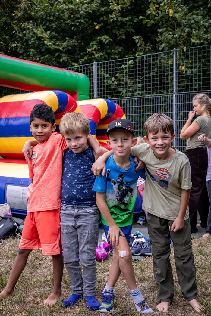 Vier lächelnde Jungen stehen nebeneinander vor einer bunten Hüpfburg.