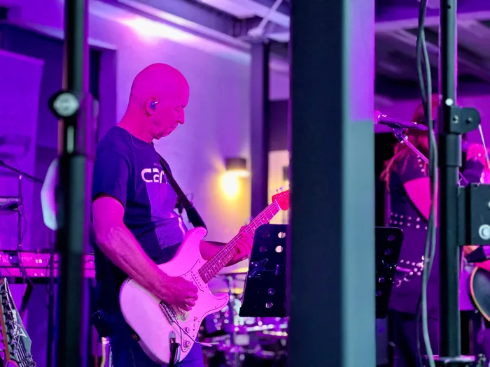 Ein Mann spielt eine weiße E-Gitarre unter violettem Bühnenlicht beim Abschiedskonzert der Band Cane.