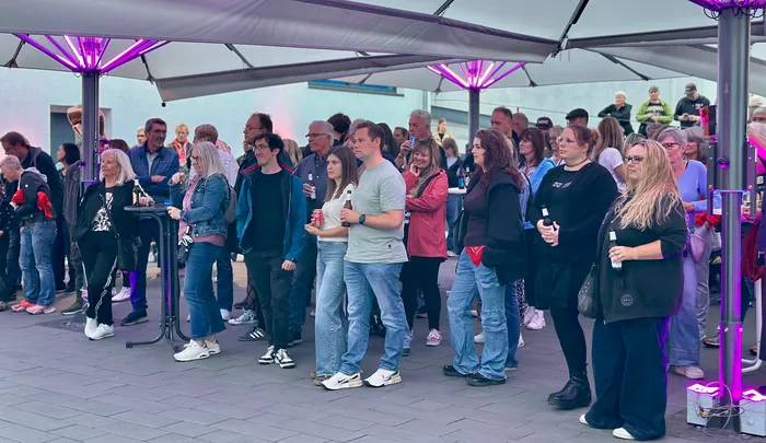 Menschen stehen bei einem Abschiedskonzert unter lila beleuchteten Sonnenschirmen.