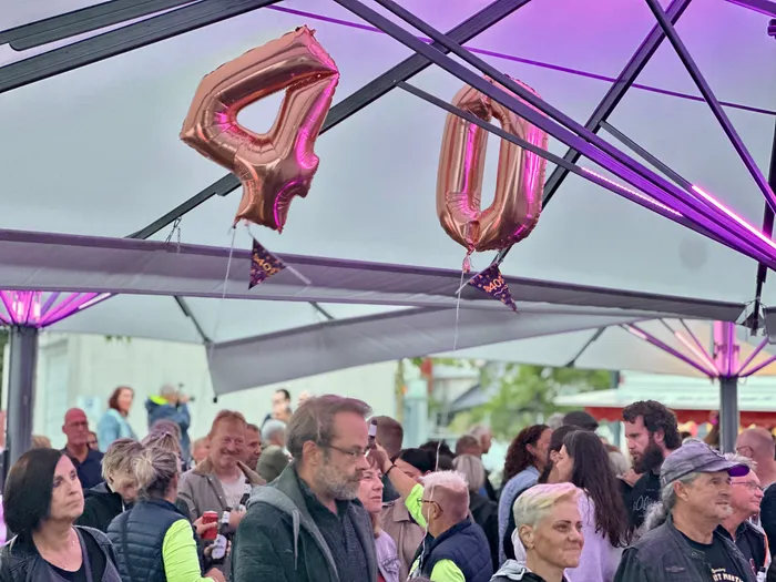 Roségoldene Folienballons in Form der Zahl 40 hängen unter einem lila beleuchteten Zeltdach über einer Menschenmenge.