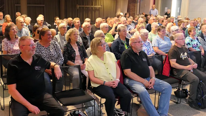 Eine große Gruppe von Menschen sitzt in Reihen auf Stühlen während eines Chorcoachings.