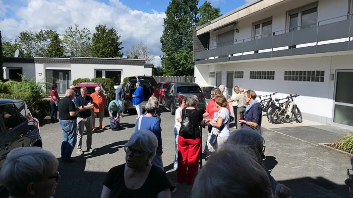 Eine Gruppe von Menschen steht in einem gepflasterten Hof vor einem weißen Gebäude.