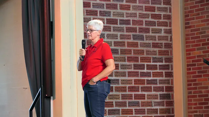 Ulrike Wahren in einem roten Poloshirt hält ein Mikrofon vor einer Ziegelwand.
