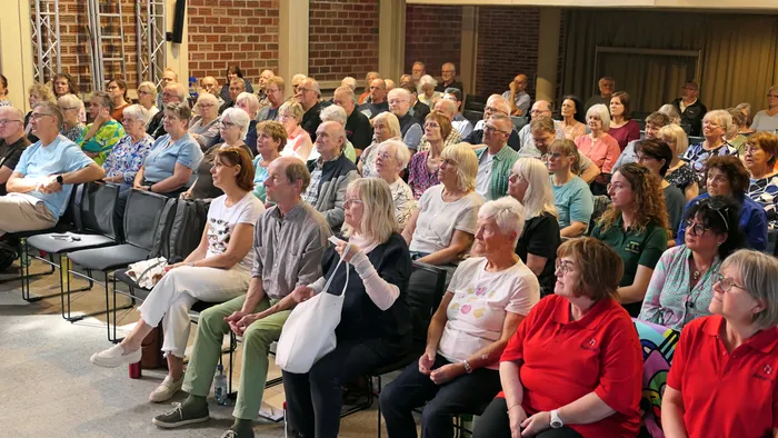 Eine große Gruppe von Chorsängern sitzt in Reihen in einem Saal während eines Coachings.