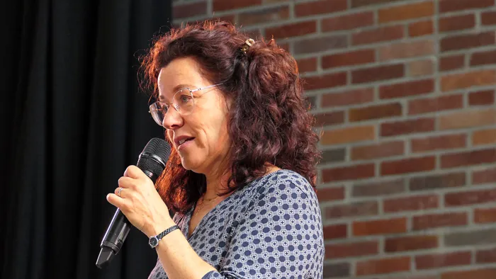 Ulrike Wahren spricht in ein Mikrofon während eines Chorcoachings vor einer Ziegelwand.