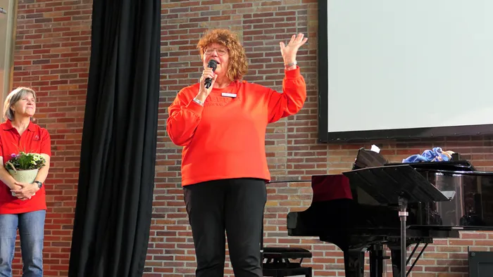 Ulrike Wahren spricht in ein Mikrofon vor einem schwarzen Flügel und einer Leinwand.