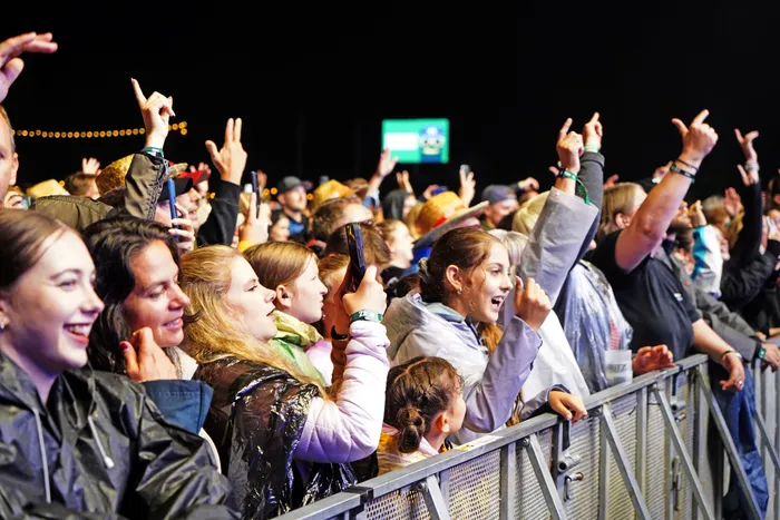 Begeisterte Menschenmenge bei einem nächtlichen Konzert, die mit erhobenen Händen vor einer Metallabsperrung jubelt.
