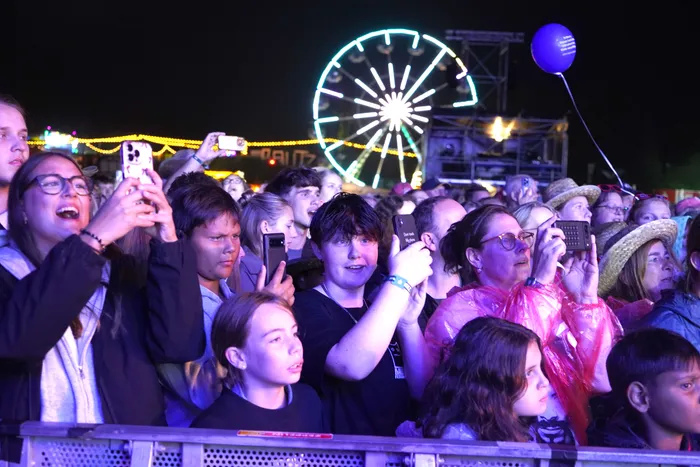 Eine Menschenmenge bei einem nächtlichen Festival fotografiert mit Smartphones, im Hintergrund ein hell erleuchtetes Riesenrad.