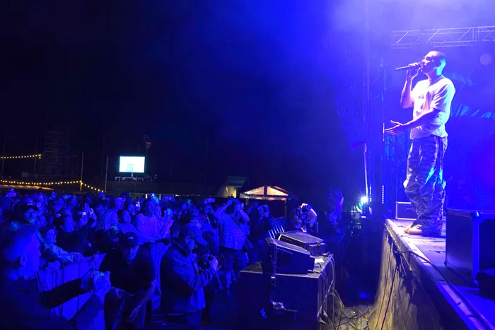 Sänger Clockclock performt unter blauem Bühnenlicht vor einer Menge, die das Konzert mit Smartphones filmt.