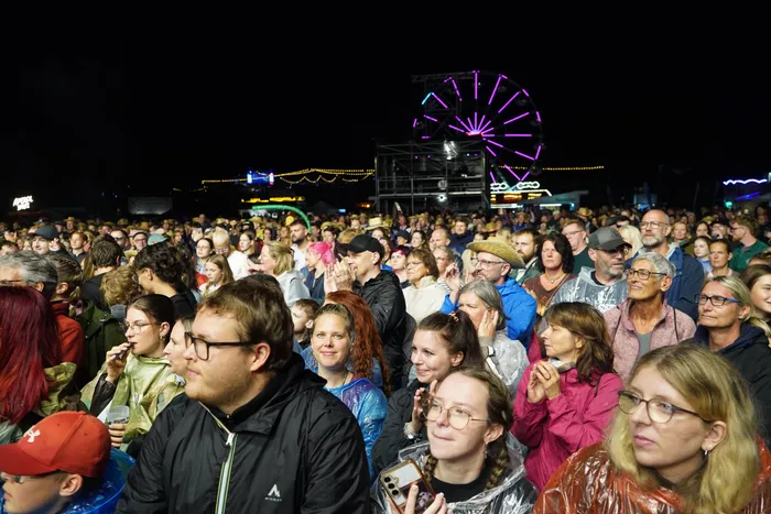 Eine große Menschenmenge bei einem nächtlichen Open-Air-Event vor einem lila beleuchteten Riesenrad.