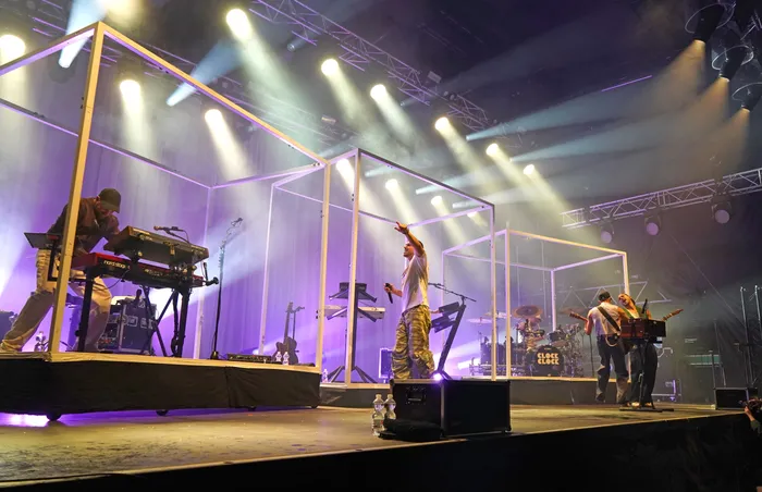 Die Band Clockclock performt auf einer Bühne mit hellen Scheinwerfern und markanten weißen Rahmenstrukturen.