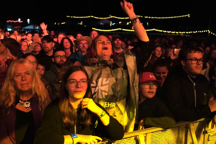 Eine begeisterte Menschenmenge bei einem nächtlichen Open-Air-Konzert, im Zentrum eine singende Frau mit erhobenem Arm.