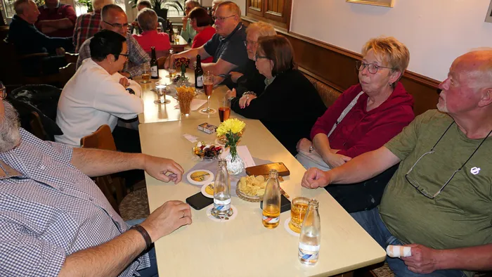 Menschen sitzen an Tischen in einer Kneipe, einige schauen in Richtung eines Comedians, der nicht im Bild zu sehen ist. Auf den Tischen stehen Getränke und Snacks.
