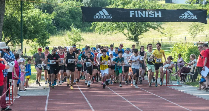 Läufer durchqueren die Ziellinie eines Crosslaufes, erkennbar an der „FINISH“-Flagge und den Startnummern der Sportler. Zuschauer säumen die Laufstrecke.