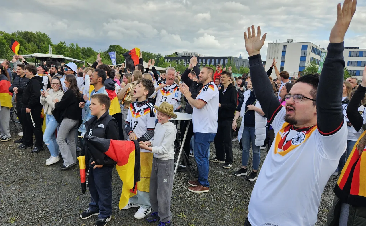 Jubelnde Menschenmenge mit Deutschlandflaggen und Trikots der Nationalmannschaft nach einem Sieg. Im Vordergrund ein Mann mit hoch erhobenen Armen.