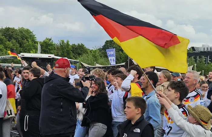Jubelnde Menschenmenge mit Deutschlandflaggen nach dem Sieg der deutschen Nationalmannschaft gegen Curaçao bei einer XXL-WM-Party. Ein Mann mit roter Kappe wird von Fans umringt und fotografiert.