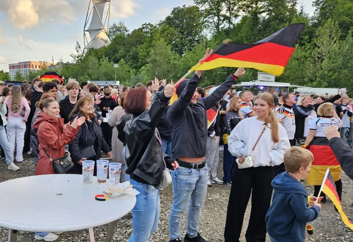 Jubelnde Menschenmenge mit Deutschlandflaggen nach dem Sieg der deutschen Nationalmannschaft gegen Curaçao bei einer Public-Viewing-Veranstaltung. Im Vordergrund eine Frau mit hochgehaltener Flagge und weitere Fans, die den Sieg bejubeln.