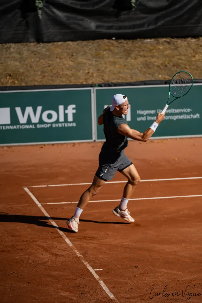 Tom Gentzsch schwingt seinen grünen Tennisschläger auf einem Sandplatz.