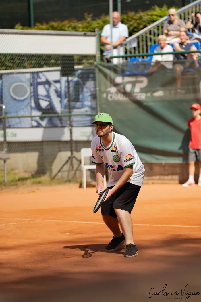 Kristians Koldvell in weißem T-Shirt und grüner Kappe steht mit dem Tennisschläger bereit auf einem Sandplatz.