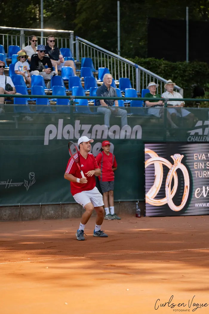 Kristian Koldvell in rotem T-Shirt und weißer Kappe steht mit einem Tennisschläger auf einem Sandplatz bei den Platzmann Open 2026.