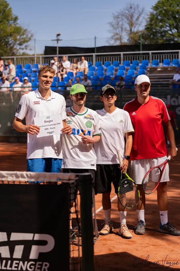 Vier Männer stehen auf einem Tennis-Sandplatz; zwei von ihnen halten einen Scheck über 500 Euro für den Sieg der One-Point-Challenge.
