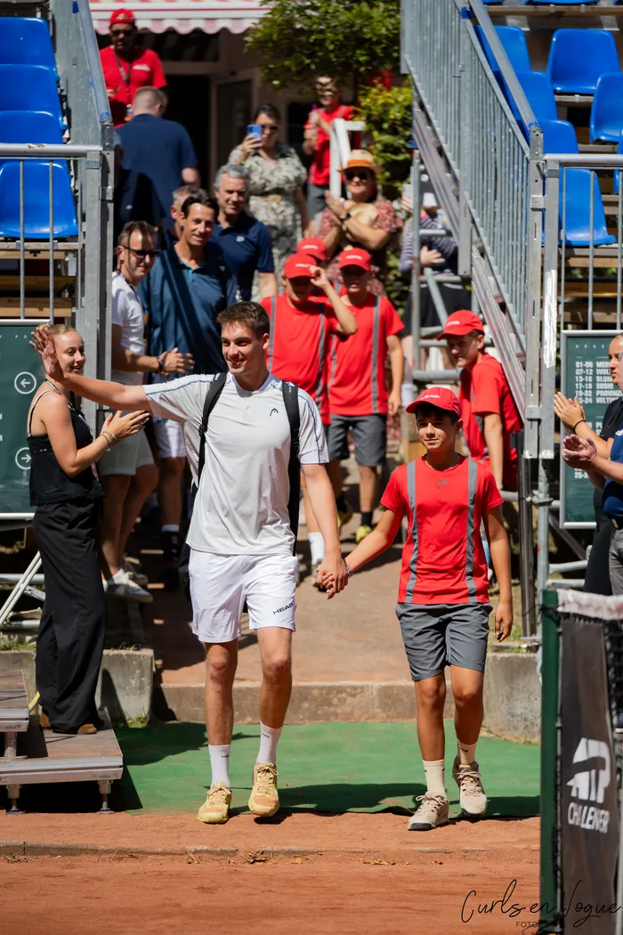 Ein Mann in weißer Sportkleidung geht Hand in Hand mit einem Jugendlichen in einem roten T-Shirt über einen Sandplatz bei den Platzmann Open 2026.