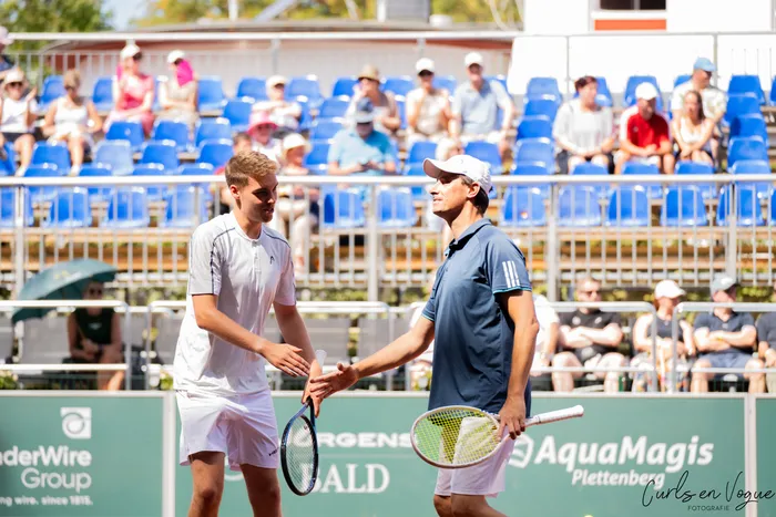 Zwei Tennisspieler schütteln sich nach einem Show-Match die Hände auf einem Tennisplatz vor einer Tribüne mit Zuschauern.