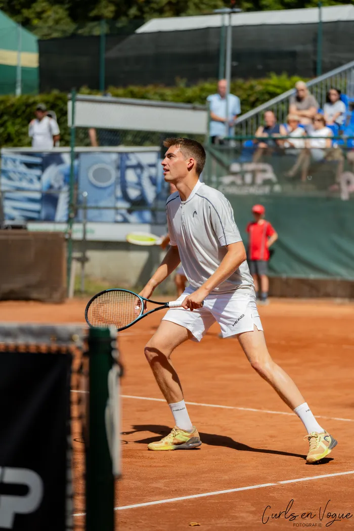 Ein Tennisspieler in weißer Sportkleidung steht mit dem Schläger bereit auf einem Sandplatz.