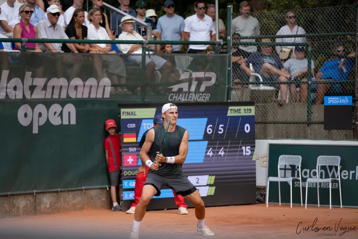 Tom Gentzsch in spielbereiter Haltung auf einem Sandplatz vor einer Anzeigetafel bei den Platzmann Open.