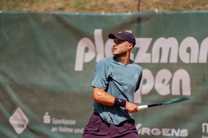 Ein Tennisspieler schlägt den Ball während eines Spiels. Im Hintergrund ist ein Werbebanner mit der Aufschrift „Ploezmar Open“ zu sehen.