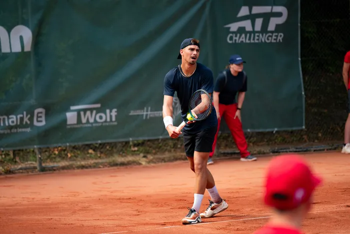 Ein Tennisspieler steht mit Schläger auf einem Sandplatz vor einem ATP Challenger Banner.