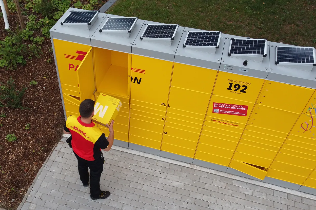 Gelbe DHL Packstation mit Solarzellen auf dem Dach, ein Mitarbeiter mit DHL-Kleidung steht davor und hält ein Paket.