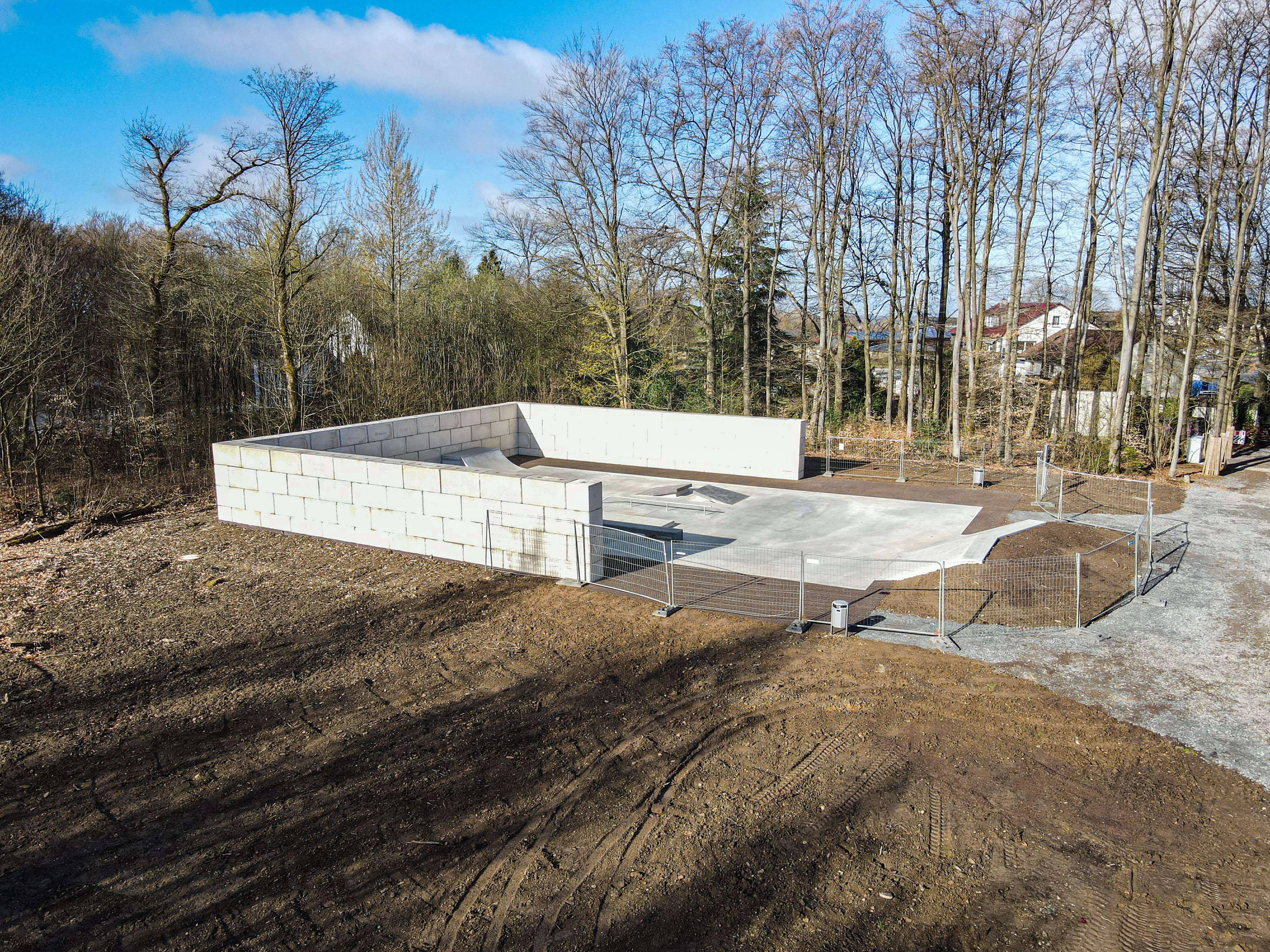 Rohbau einer Skate- und Bikeanlage mit Betonfundament und Mauerwerk, umgeben von Bauzaun und freier Fläche.
