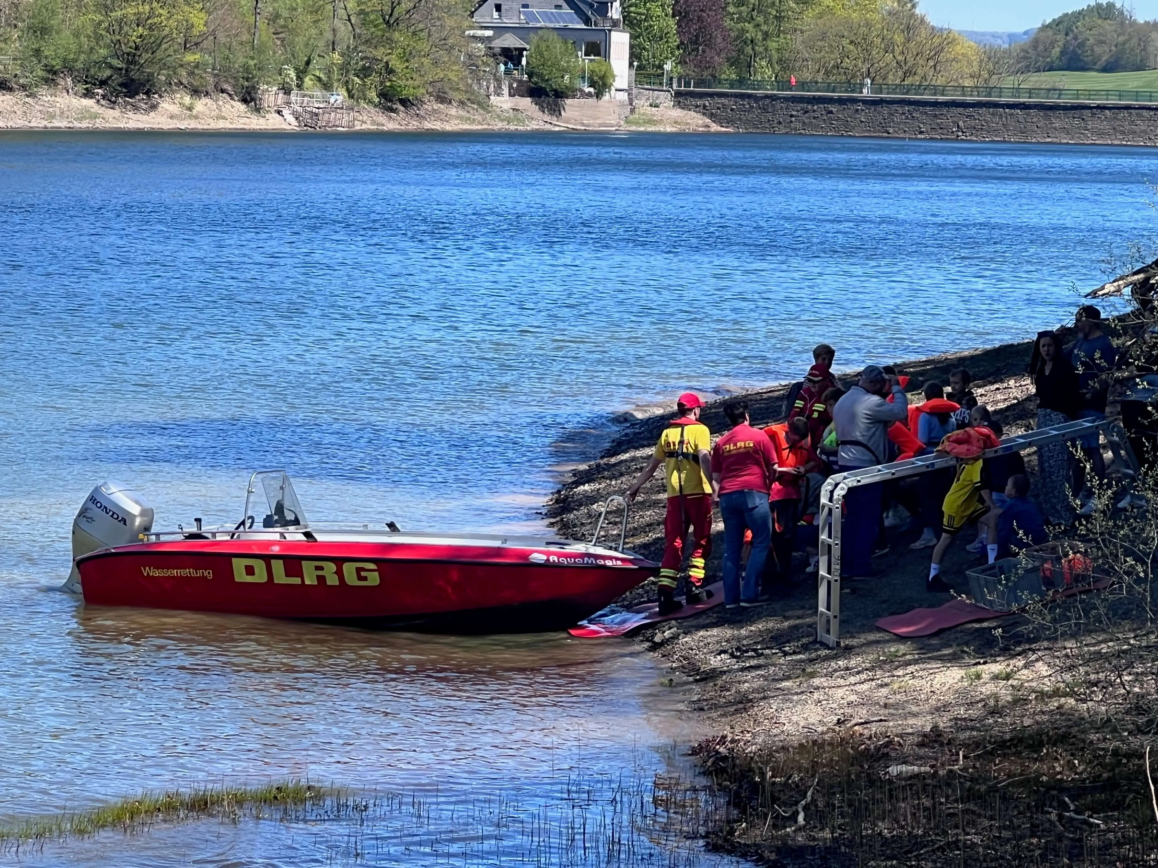 Rettungskräfte der DLRG helfen Menschen an einer Steganlage am Ufer der Oestertalsperre, ein rotes Rettungsboot liegt im Wasser.
