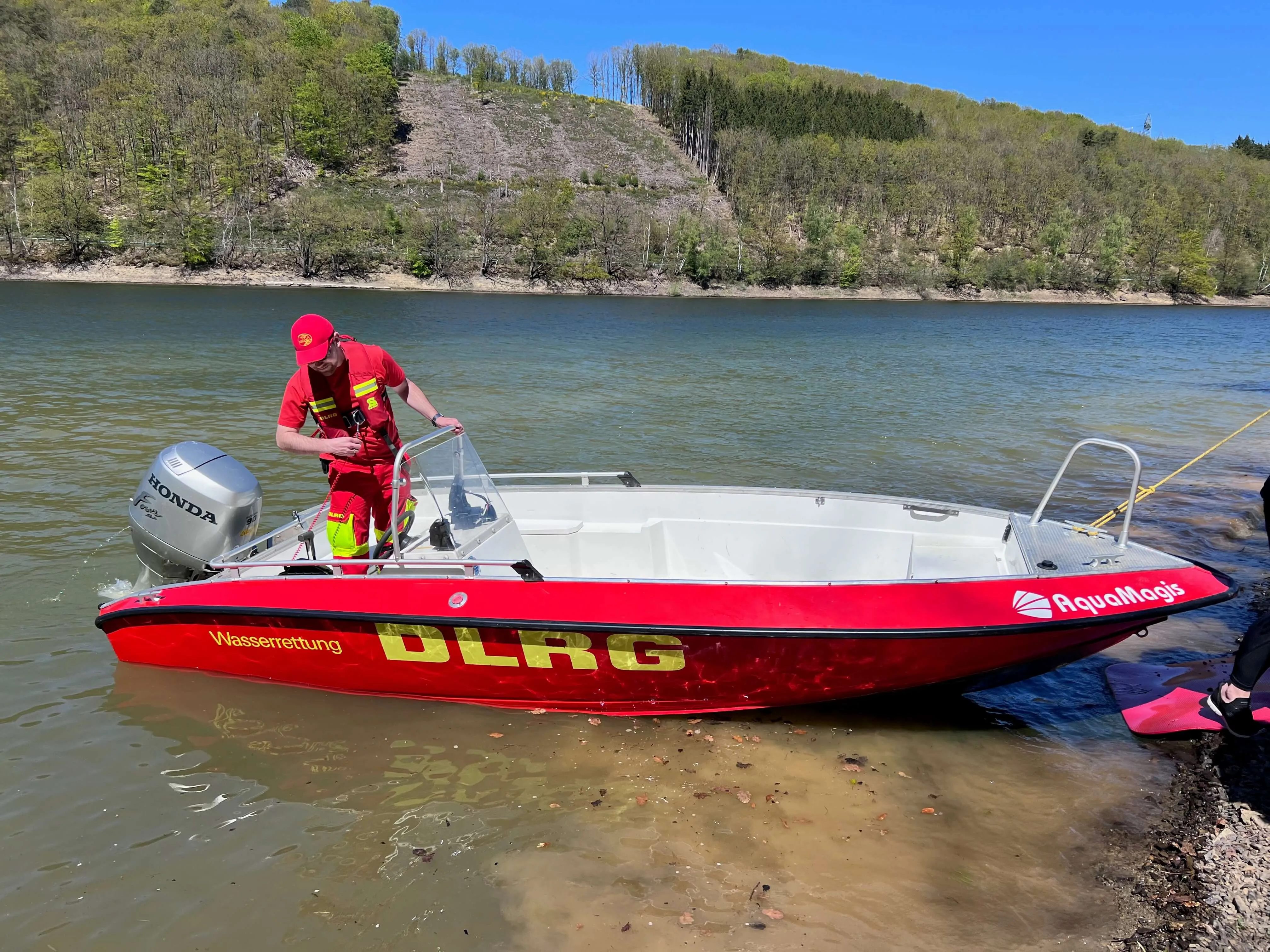 Rotes DLRG-Rettungsboot mit Honda-Motor liegt am Ufer der Oestertalsperre. Ein Retter in roter Kleidung bereitet das Boot vor.