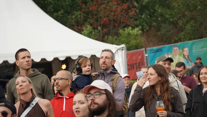 Eine Gruppe von Menschen blickt bei einem Event vor einem großen weißen Zelt in Richtung einer Bühne.