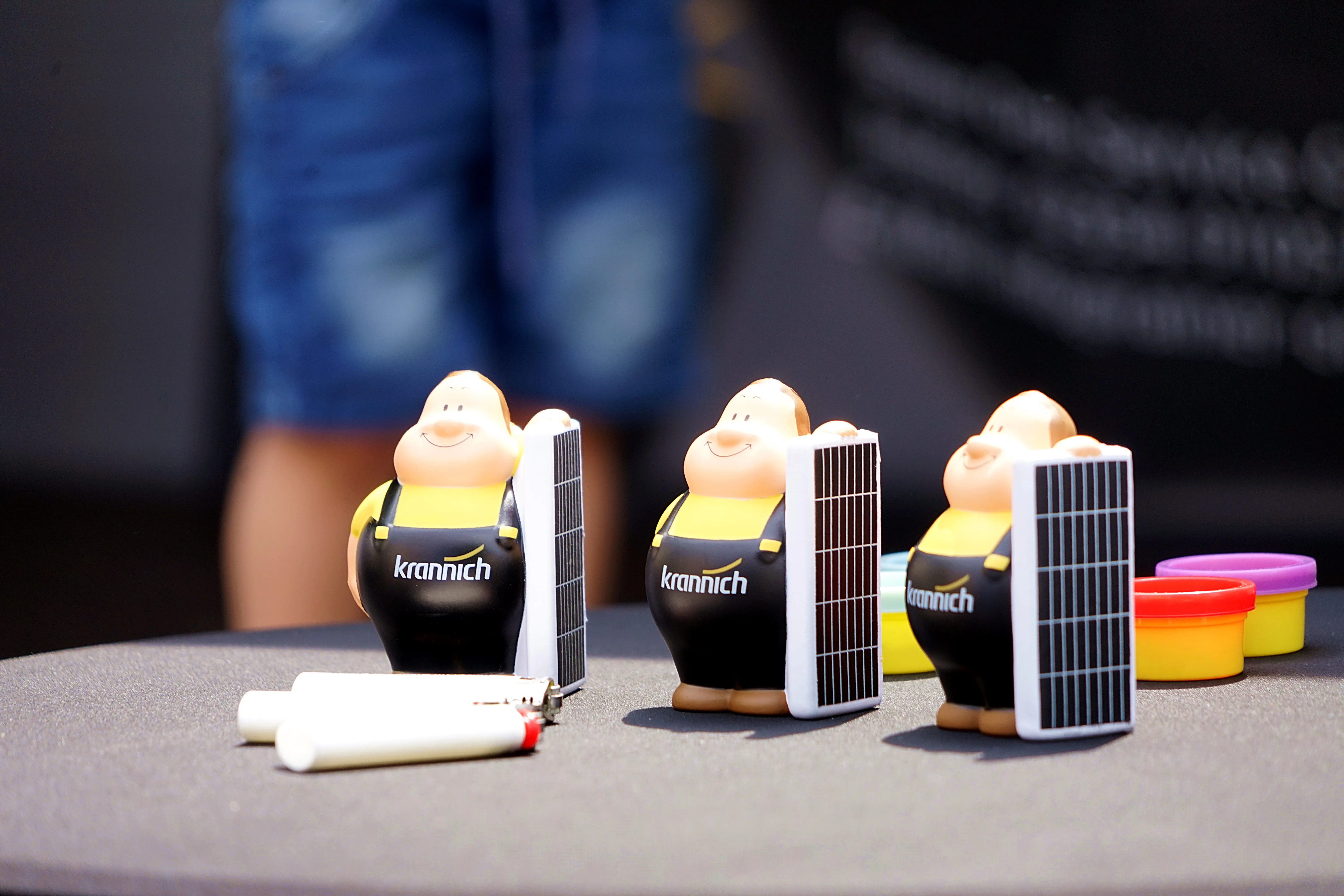Drei schwarze Figuren mit gelben Köpfen und dem Aufdruck „krannich“ tragen kleine Solarzellen auf dem Rücken.