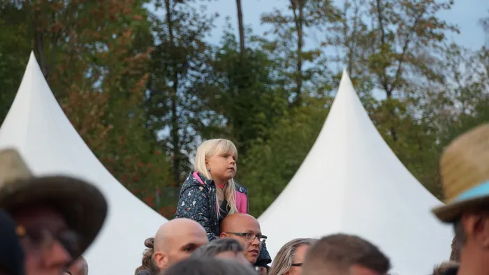 Ein blondes Mädchen blickt in einer Menschenmenge vor großen weißen Zelten zur Seite.