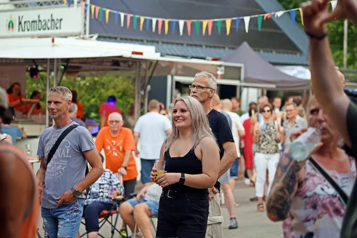 Menschen stehen auf einem Festivalgelände zusammen, im Hintergrund ein Stand mit dem Schriftzug 